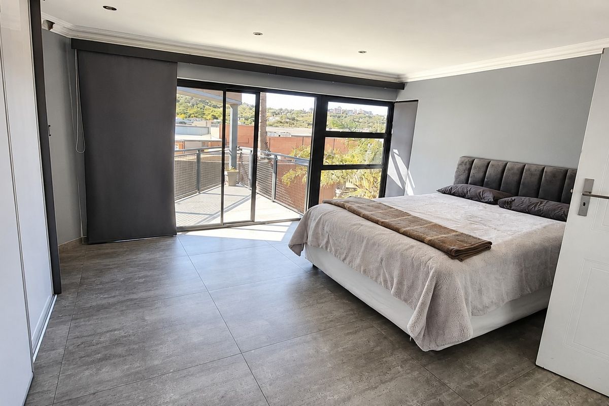 Spacious bedroom featuring modern grey floor tiles, built-in cupboards, and large sliding glass doors leading to a private balcony with scenic views.