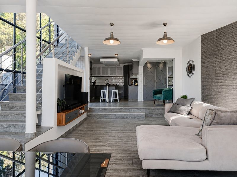 Spacious open-plan living area featuring a modern kitchen, stone accent wall, and a striking staircase with large windows, creating a bright and contemporary atmosphere.