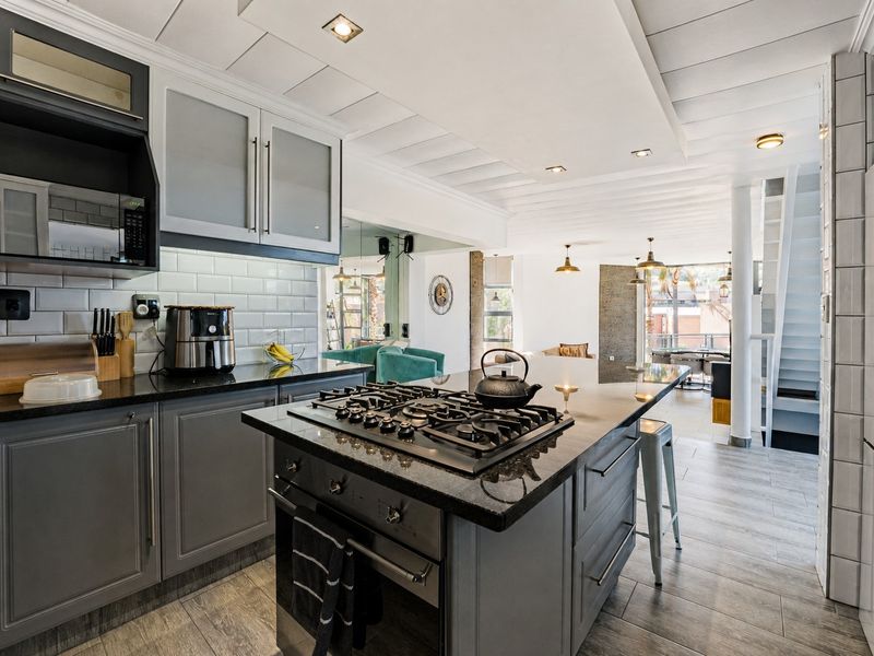 Modern open-plan kitchen featuring a central island with gas cooktop, granite countertops, and subway tile backsplash, flowing into the living and dining area.