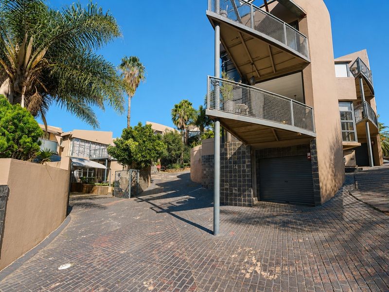 Front exterior view of a townhouse featuring a paved driveway, integrated garage, and multi-level balconies with metal railings.