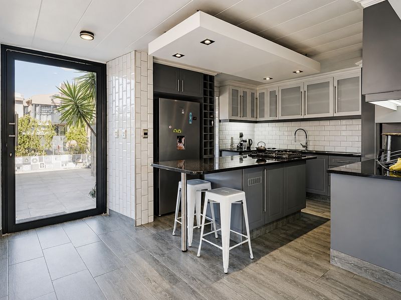 Modern kitchen featuring dark grey cabinetry, granite countertops, subway tile backsplash, and a central island with gas hob, opening onto an outdoor patio area.