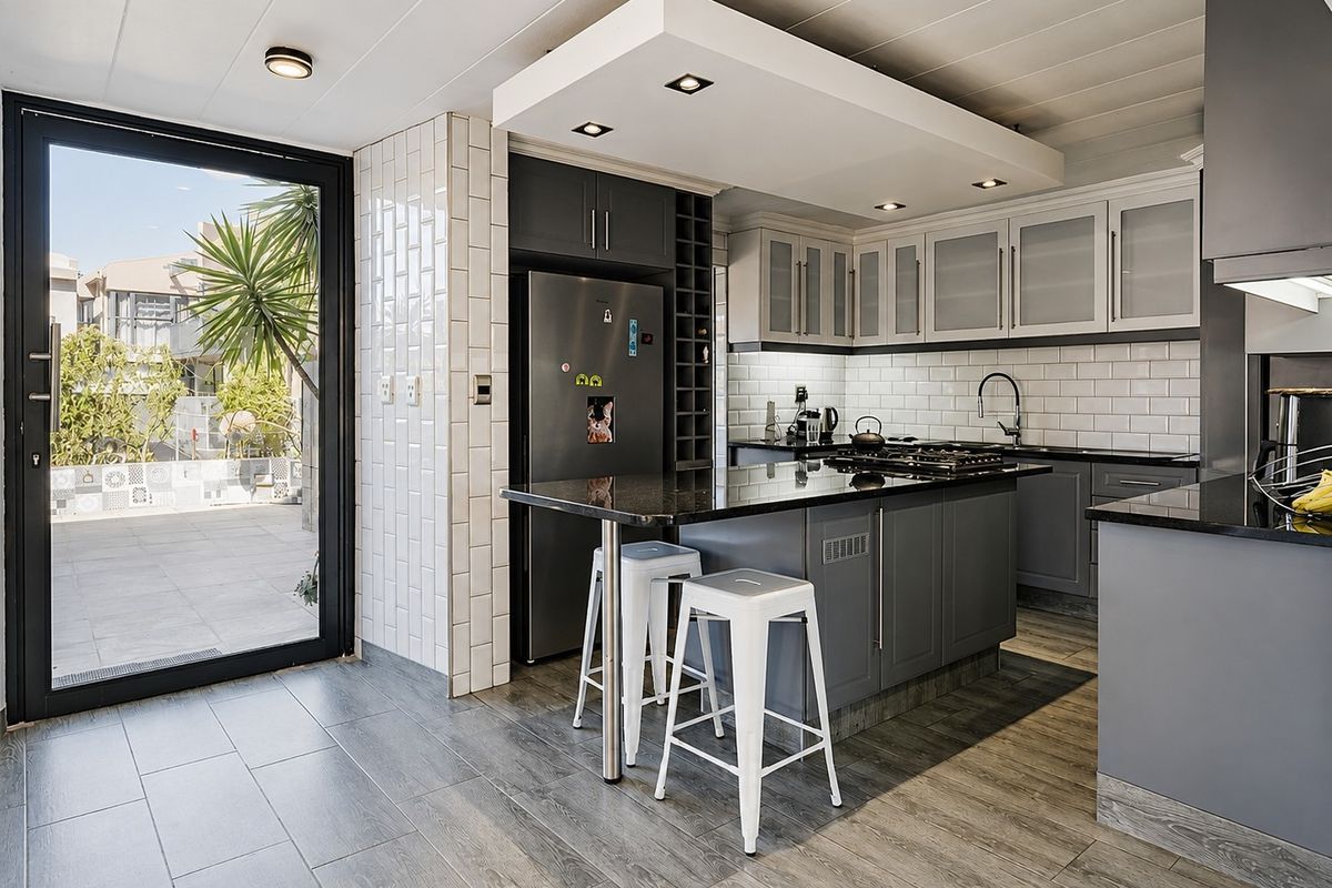 Modern kitchen featuring dark grey cabinetry, granite countertops, subway tile backsplash, and a central island with gas hob, opening onto an outdoor patio area.