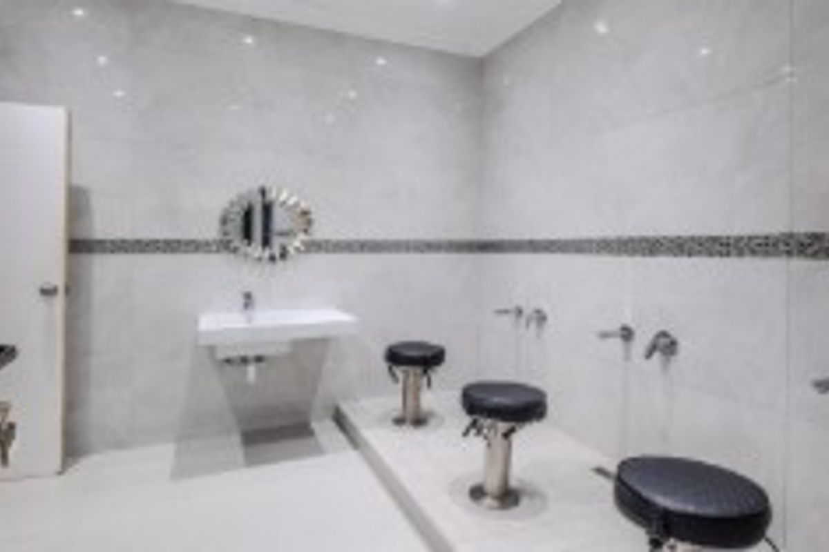 A modern, tiled bathroom or salon-style space featuring a wall-mounted basin, raised platform, and clean, neutral finishes throughout.