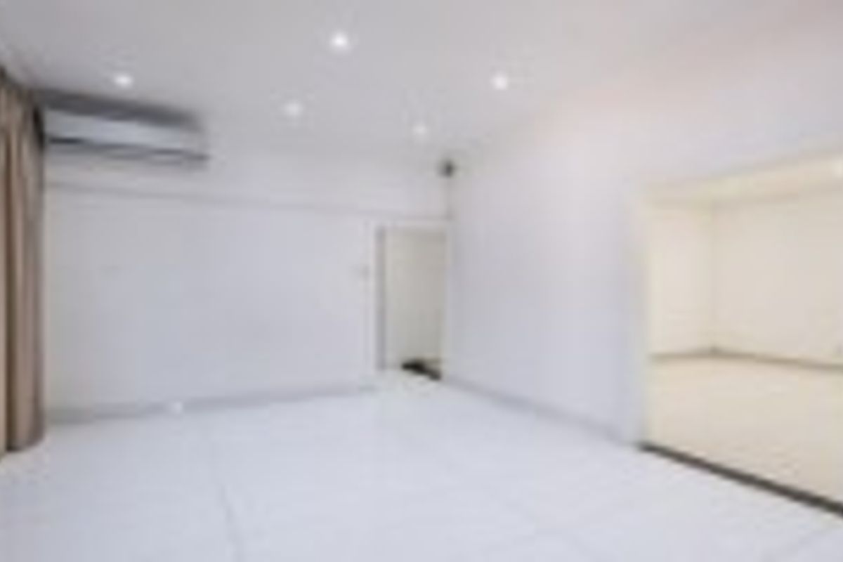 A bright, empty living area featuring white tiled flooring, recessed downlighting, and a wall-mounted split-system air conditioning unit.
