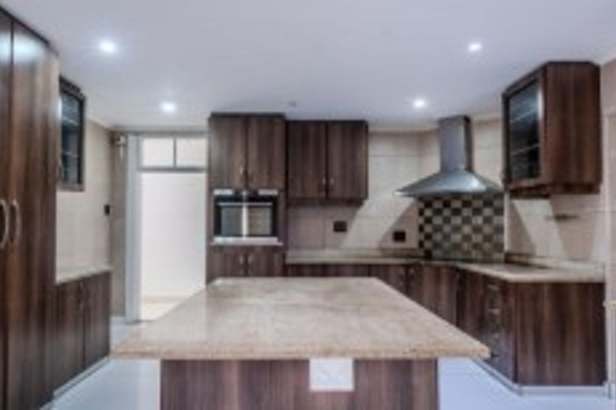 A spacious kitchen featuring dark wood cabinetry, a large central island with stone countertops, built-in oven, and a stainless steel extractor fan.