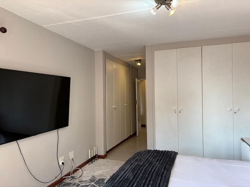 A bedroom featuring neutral wall tones, tiled flooring, and extensive built-in cupboard storage, providing a functional and clean living space.