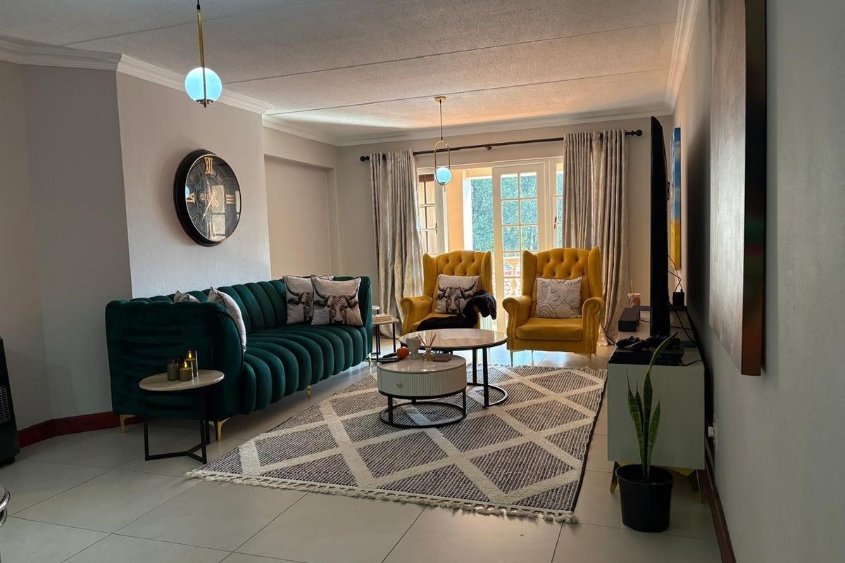A well-lit living room featuring neutral tiled flooring, decorative cove cornicing, and glass-paned french doors leading to an outdoor area.
