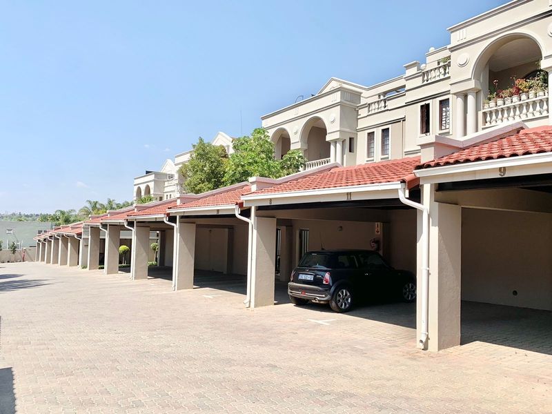 A row of covered parking bays featuring terracotta roof tiles and concrete pillars, situated within a well-maintained apartment complex.