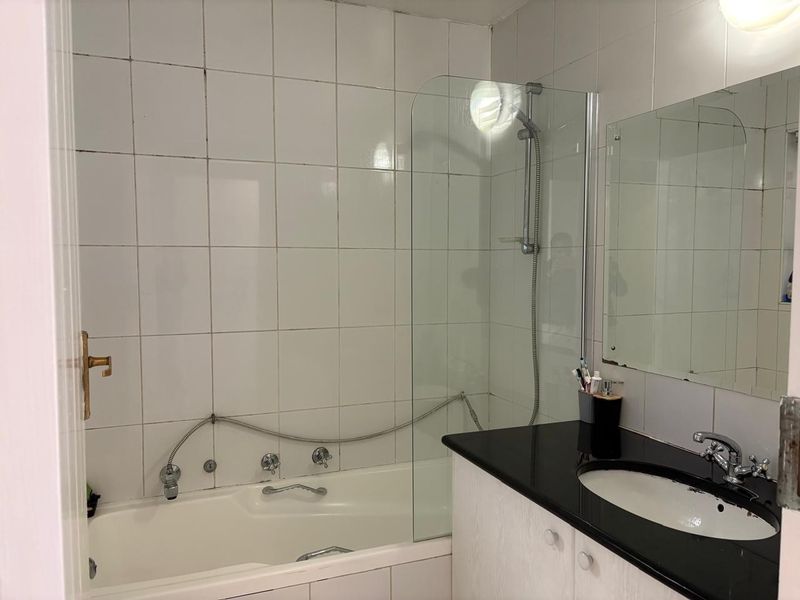 A functional bathroom featuring a built-in bathtub with a glass shower screen, a vanity cabinet with a granite countertop, and an undermount sink.