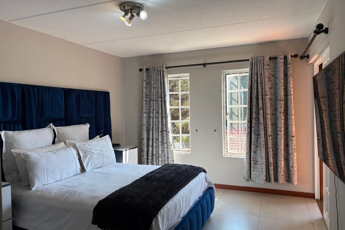 A well-maintained bedroom featuring tiled flooring, dual multi-pane windows, and a central ceiling light fixture.