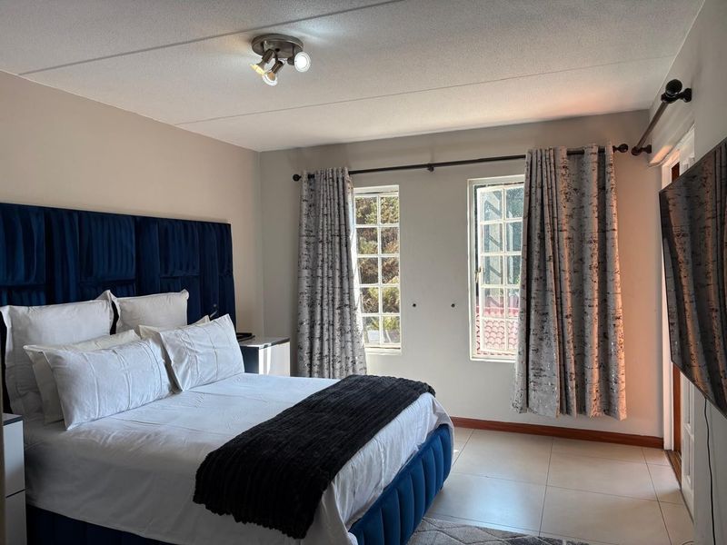 A well-maintained bedroom featuring tiled flooring, dual multi-pane windows, and a central ceiling light fixture.
