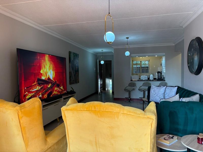 Open-plan living area featuring tiled flooring, coved ceilings, modern pendant lighting, and a breakfast bar connecting to the kitchen space.