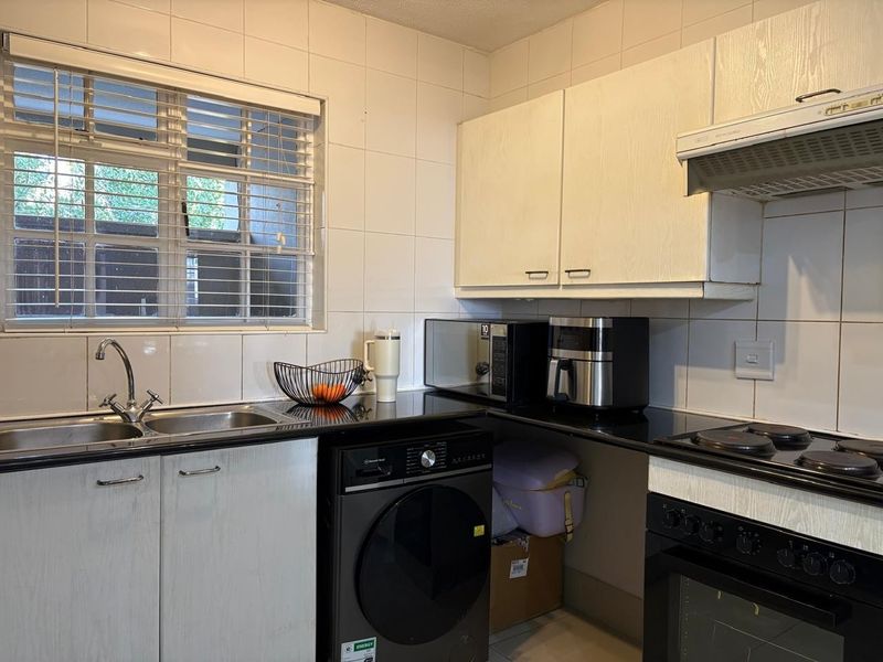 Functional kitchen featuring black granite countertops, built-in cabinetry, integrated oven and hob, and a tiled splashback with a window for natural light.