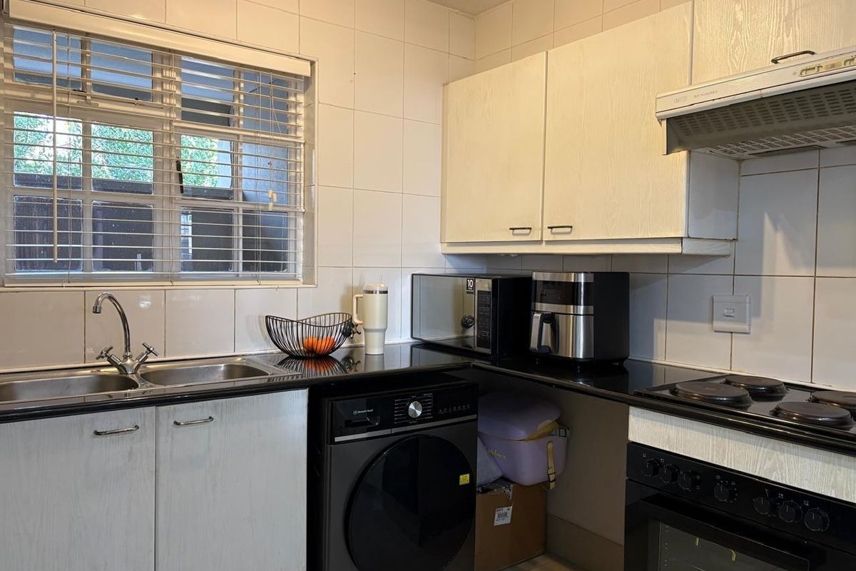 Functional kitchen featuring black granite countertops, built-in cabinetry, integrated oven and hob, and a tiled splashback with a window for natural light.