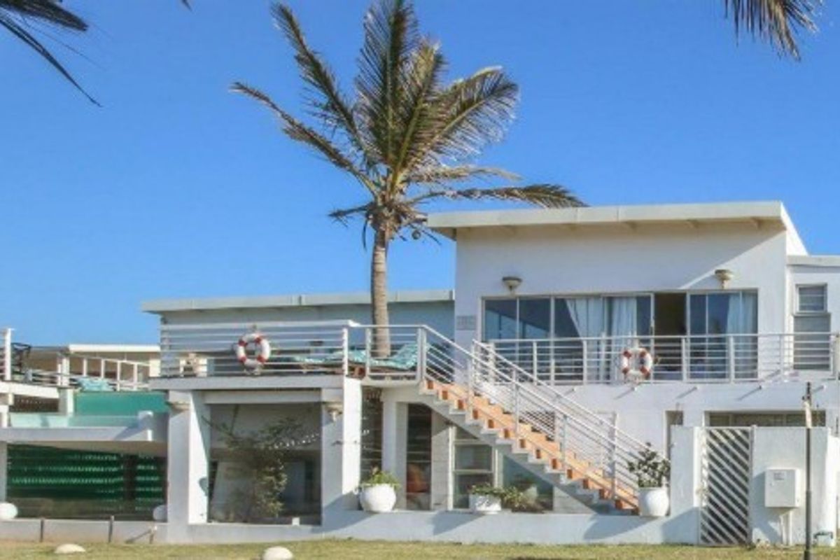 Rear view of a multi-level coastal home featuring a spacious balcony, external staircase, and large sliding glass doors overlooking the garden.