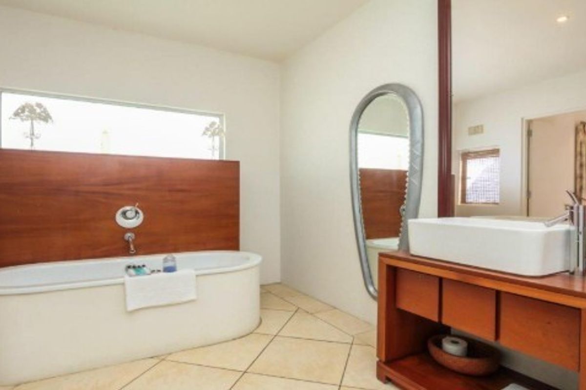 Modern bathroom featuring a sleek freestanding bathtub with wood-panel accent wall, vessel sink on a wooden vanity, and large mirror.