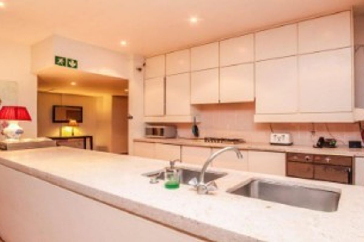 A functional kitchen featuring extensive built-in cabinetry, stone countertops, a double sink, and integrated appliances including an oven and hob.