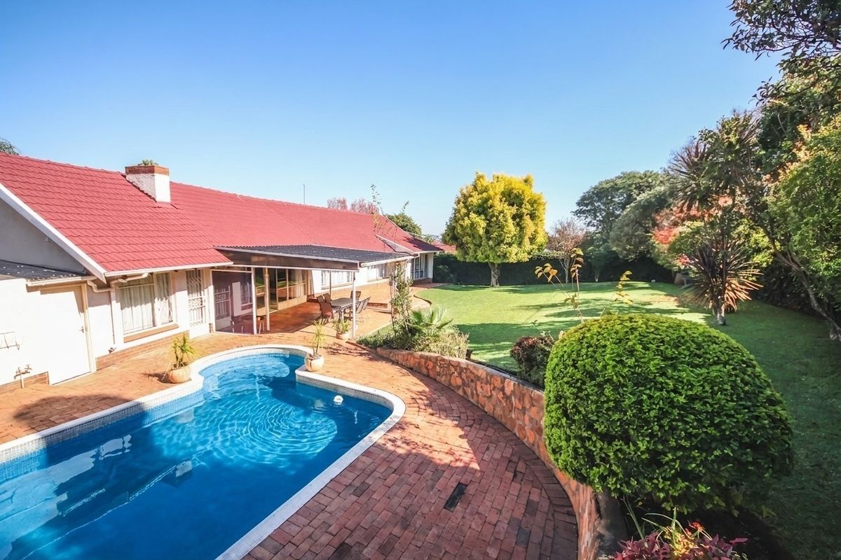 Spacious rear garden featuring a swimming pool, brick-paved patio area, covered outdoor space, and established landscaping.