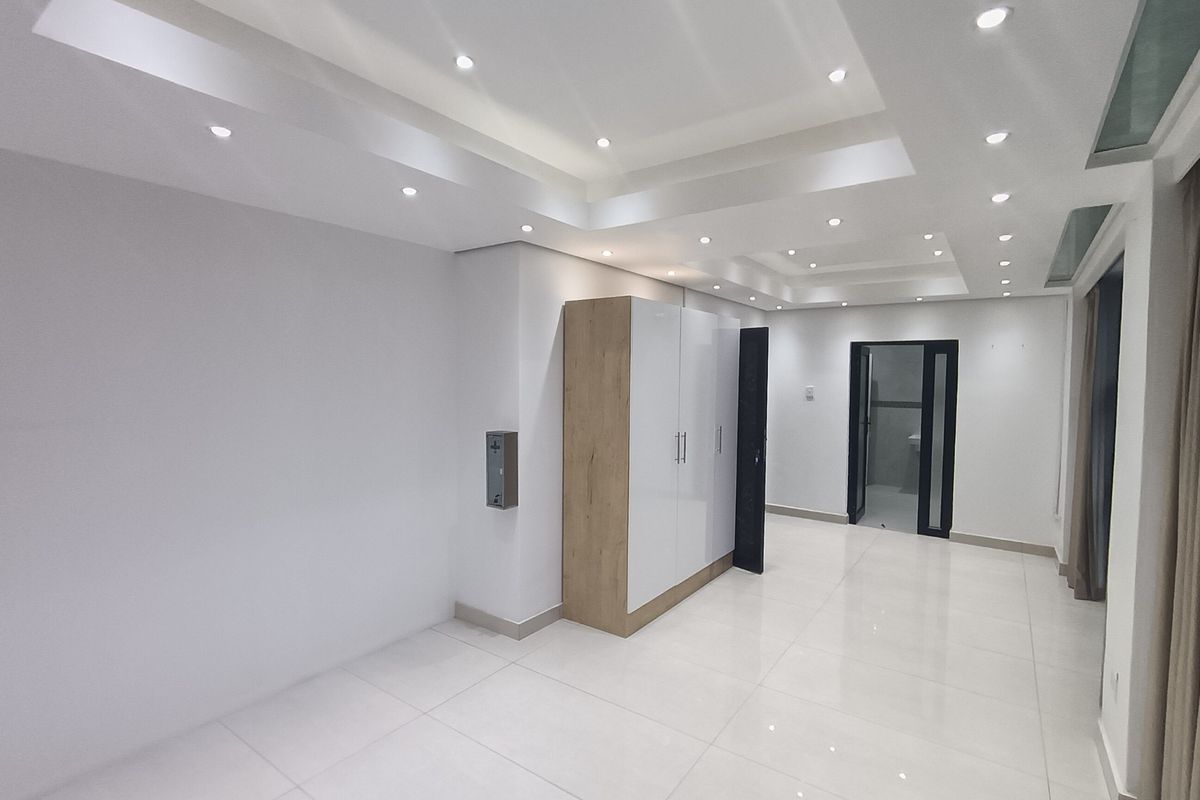 A bright, modern bedroom featuring a coffered ceiling with recessed lighting, polished tiled floors, and a sleek built-in wardrobe.