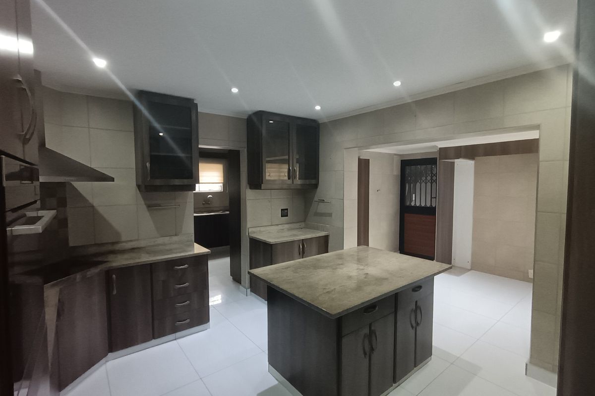 Modern kitchen featuring dark wood cabinetry, a central island with stone countertops, tiled flooring, and integrated extractor fan, offering a clean and functional workspace.