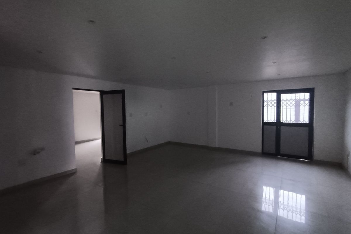 A spacious, empty living area featuring tiled flooring, recessed downlights, and a secure external door with a metal security gate.