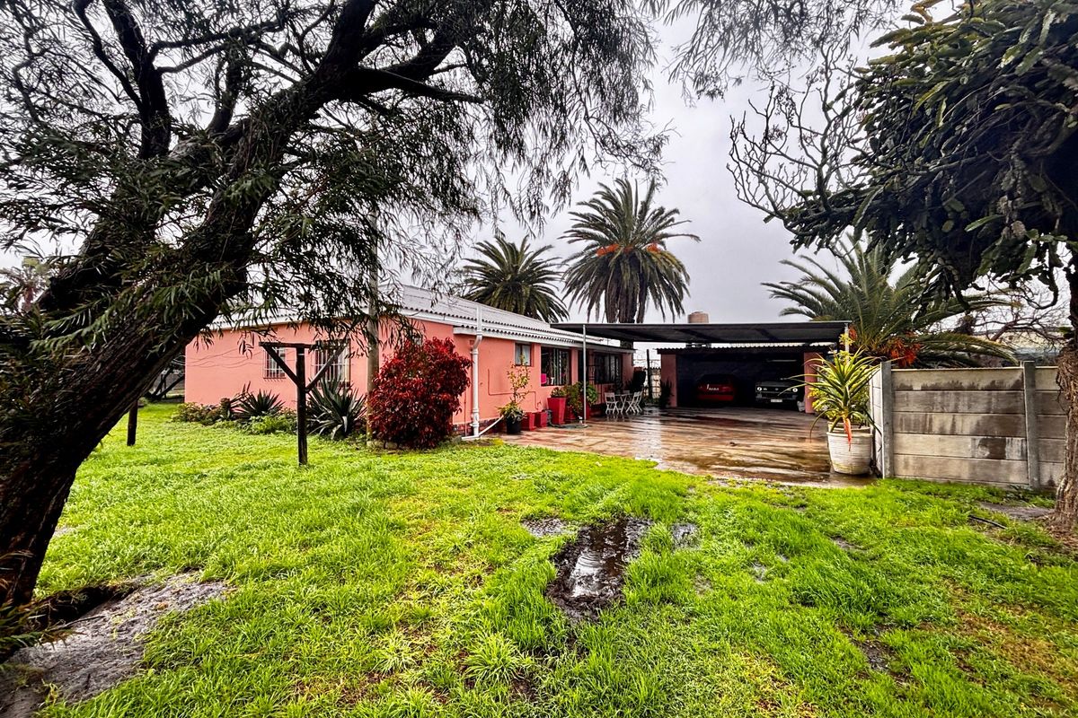 Rear view of the farm property featuring a pink exterior, a large carport, and a spacious lawn area with mature trees.
