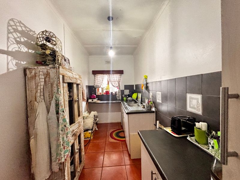 A narrow galley-style kitchen featuring tiled flooring, a stainless steel sink, and dark tiled backsplash with built-in cabinetry.