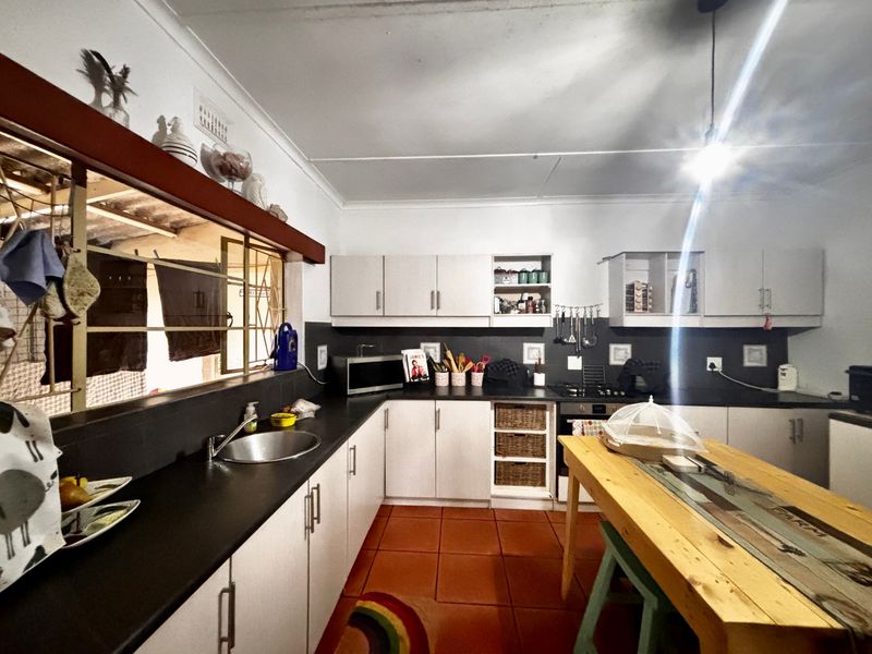 A functional kitchen featuring built-in cabinetry, dark countertops, a built-in oven, and tiled flooring, with an open-plan layout and direct access to an outdoor area.