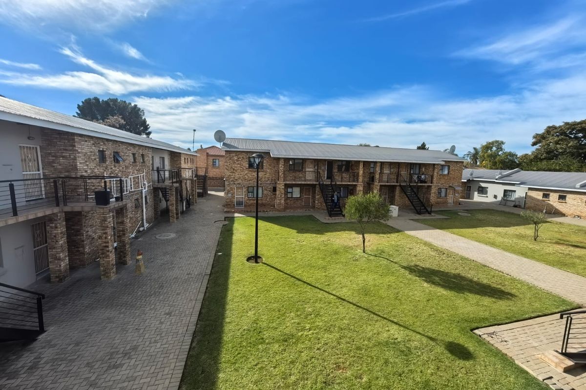 A view of the apartment complex exterior featuring brick facades, paved walkways, communal green space, and external metal staircases.