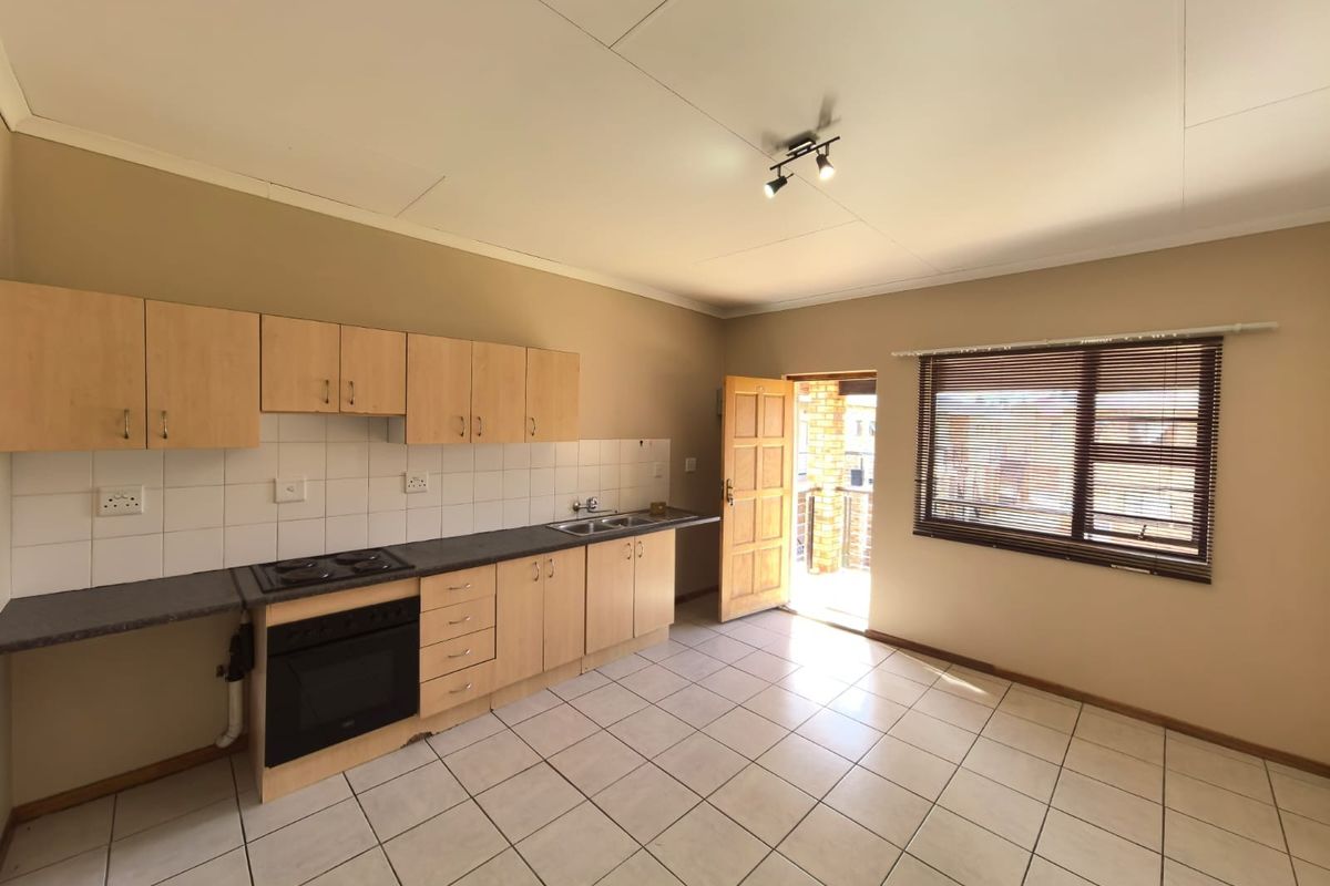 A functional kitchen featuring light wood cabinetry, laminate countertops, built-in oven and hob, and tiled flooring with direct access to an outdoor balcony.