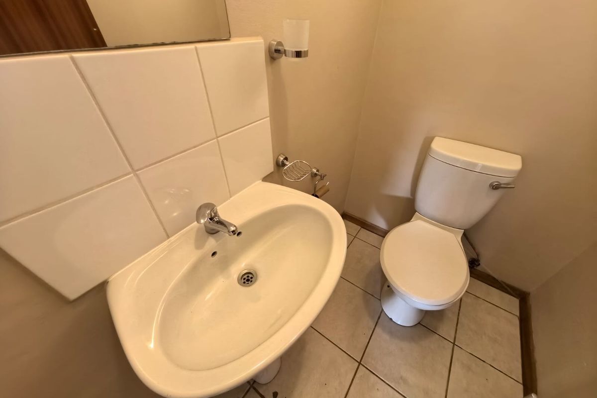 A functional bathroom featuring a pedestal washbasin, toilet, tiled splashback, and tiled flooring, providing a clean and practical space.