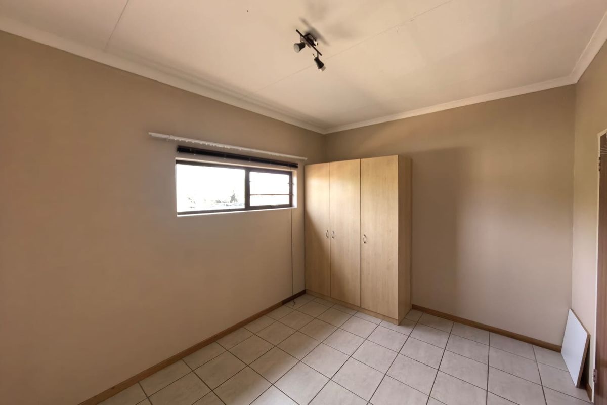 A clean, empty bedroom featuring neutral wall tones, tiled flooring, and a built-in wooden wardrobe.
