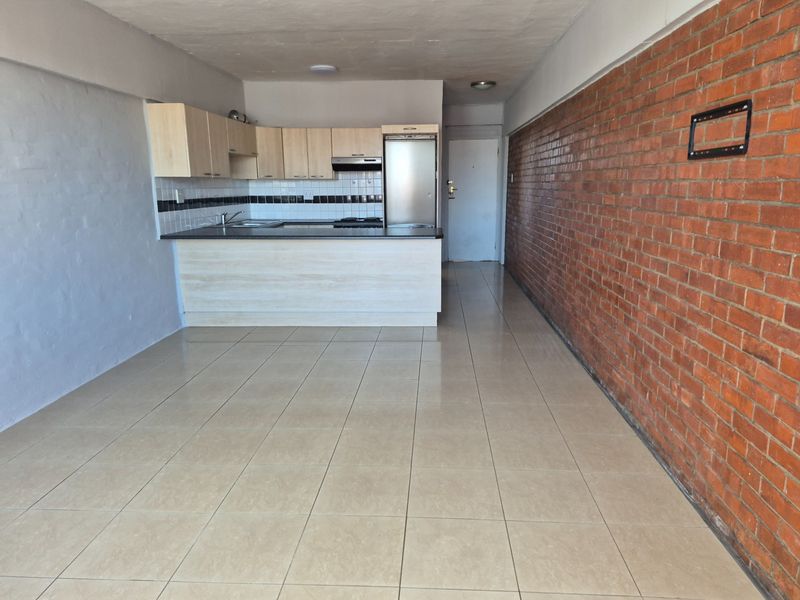 Open-plan living area featuring a functional kitchen with built-in cabinetry, tiled flooring, and a prominent exposed brick feature wall.