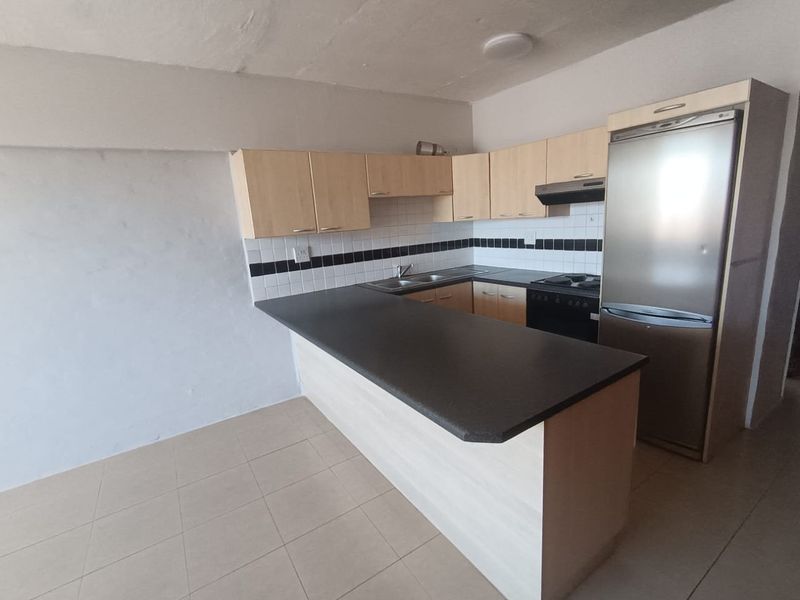 A functional kitchen featuring laminate cabinetry, dark countertops, a tiled backsplash, and built-in cooking appliances, presented in a clean, empty space.