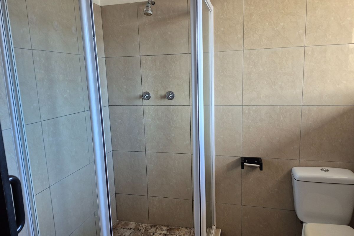 A functional bathroom featuring a shower enclosure with tiled walls and a standard toilet, requiring some maintenance to the shower floor.