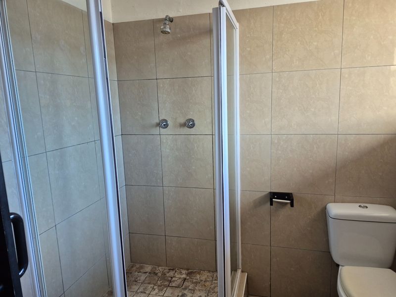 A functional bathroom featuring a shower enclosure with tiled walls and a standard toilet, requiring some maintenance to the shower floor.