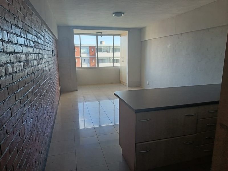 An open-plan living area featuring an exposed brick feature wall, tiled flooring, and built-in cabinetry with a countertop.
