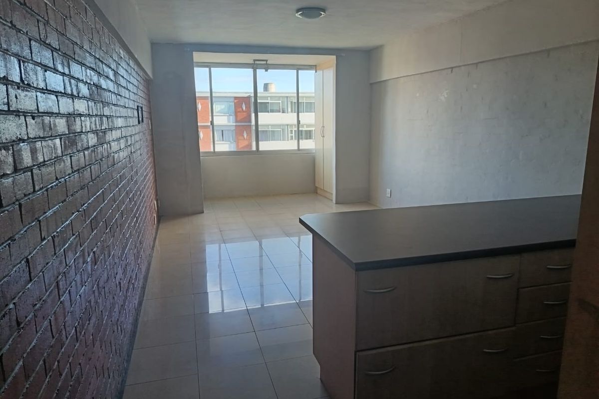 An open-plan living area featuring an exposed brick feature wall, tiled flooring, and built-in cabinetry with a countertop.
