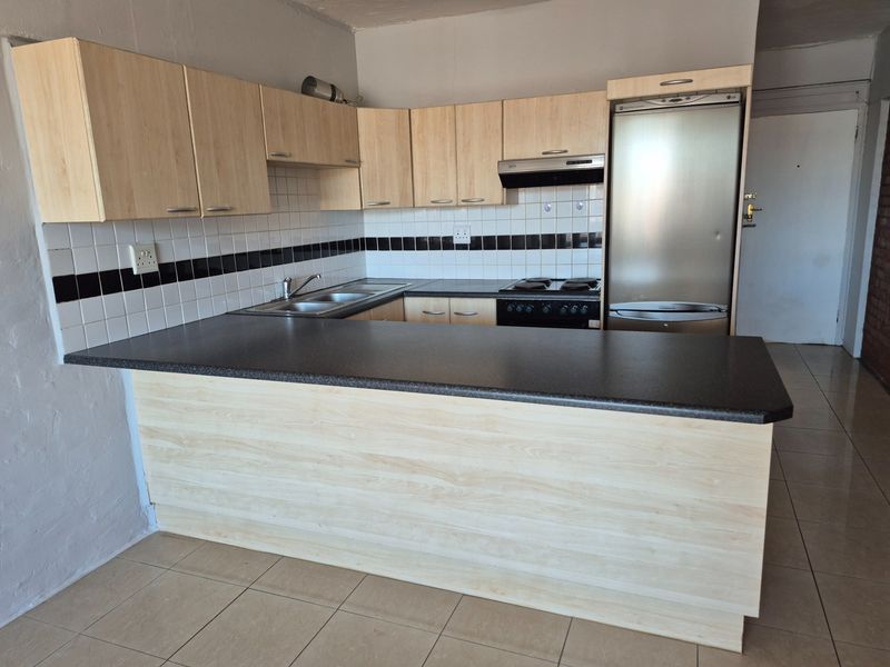 A functional kitchen featuring light wood-look cabinetry, dark laminate countertops, a double basin sink, and integrated appliances with a tiled backsplash.