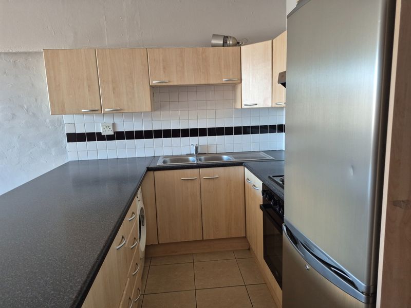 Compact kitchen featuring light wood-look cabinetry, dark laminate countertops, a tiled backsplash, and integrated oven, offering a functional layout for an apartment.