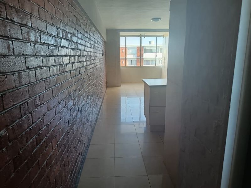 An open-plan living area featuring a striking exposed brick wall, polished tiled flooring, and a built-in kitchen island with natural light.