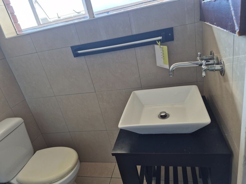 A compact bathroom featuring a modern square vessel sink with wall-mounted tapware, neutral wall tiling, and a standard toilet.