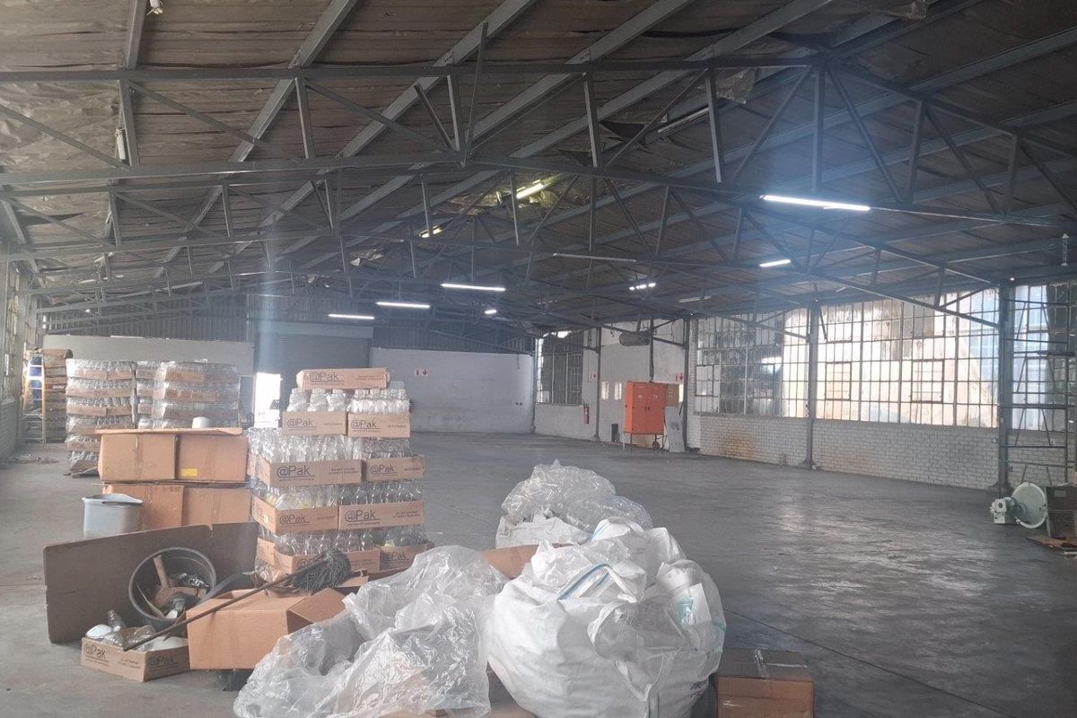 Large industrial warehouse space featuring exposed steel roof trusses, expansive steel-framed windows, and concrete flooring, suitable for storage or manufacturing operations.