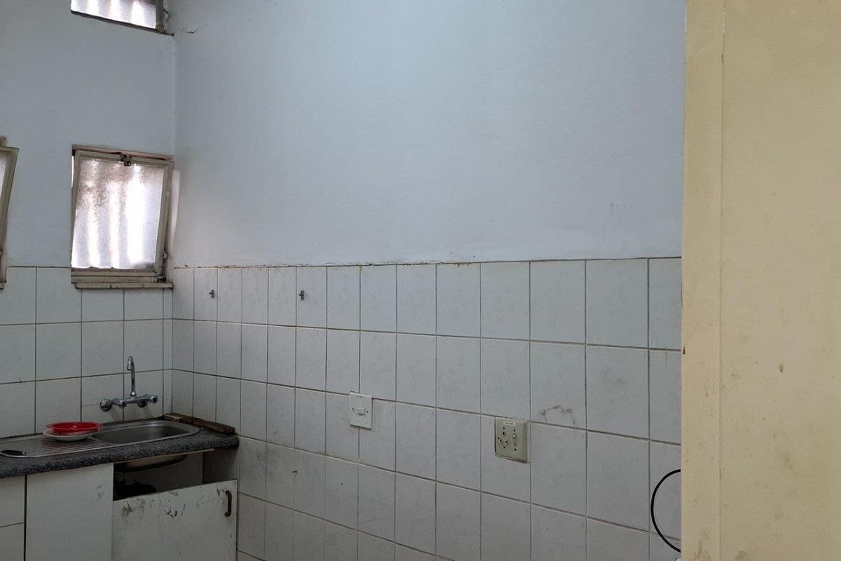 A functional kitchen area featuring a stainless steel sink, tiled splashback, and built-in cabinetry, requiring cosmetic updates and repairs to the existing fixtures.