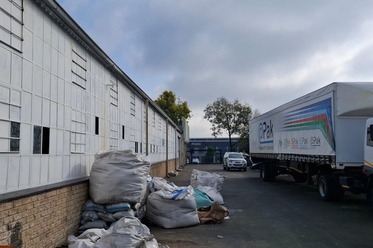 Rear industrial yard area featuring metal-clad warehouse walls with brick base and asphalt surfacing, suitable for logistics and storage operations.