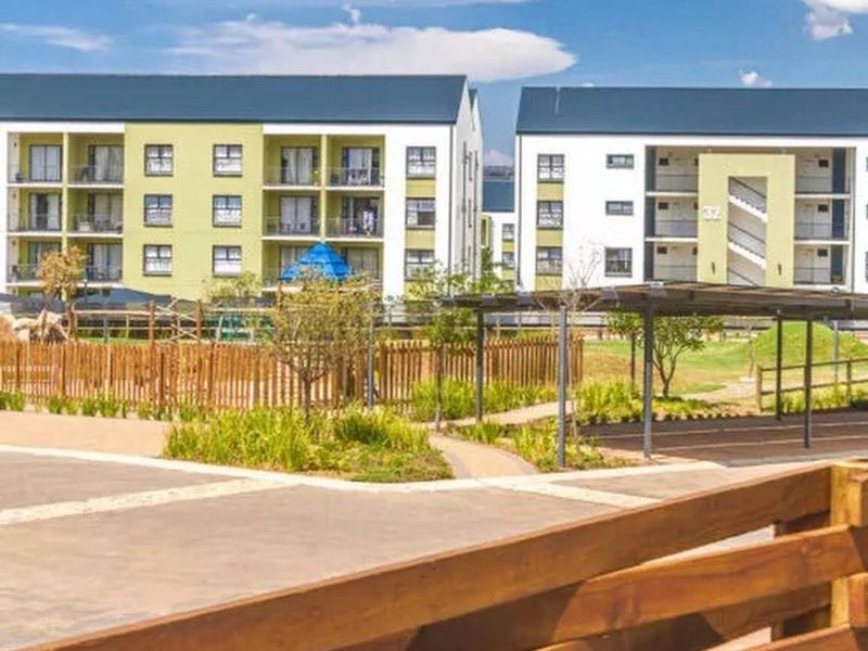 Exterior view of modern apartment blocks featuring landscaped gardens, paved walkways, and covered parking facilities within a well-maintained residential complex.