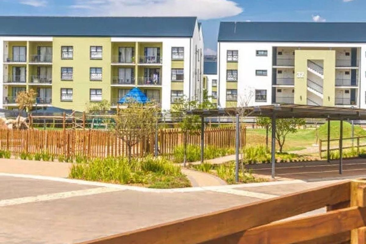 Exterior view of modern apartment blocks featuring landscaped gardens, paved walkways, and covered parking facilities within a well-maintained residential complex.