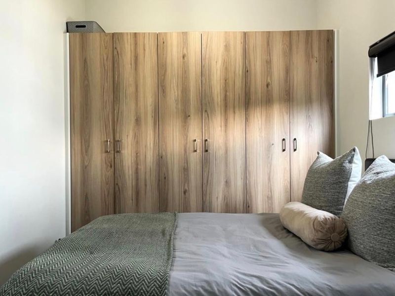A well-maintained bedroom featuring floor-to-ceiling wood-finish built-in wardrobes and a modern roller blind.