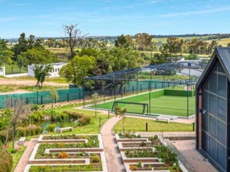 Elevated view overlooking a well-maintained landscaped garden, pond, and a fenced sports facility within the estate grounds.