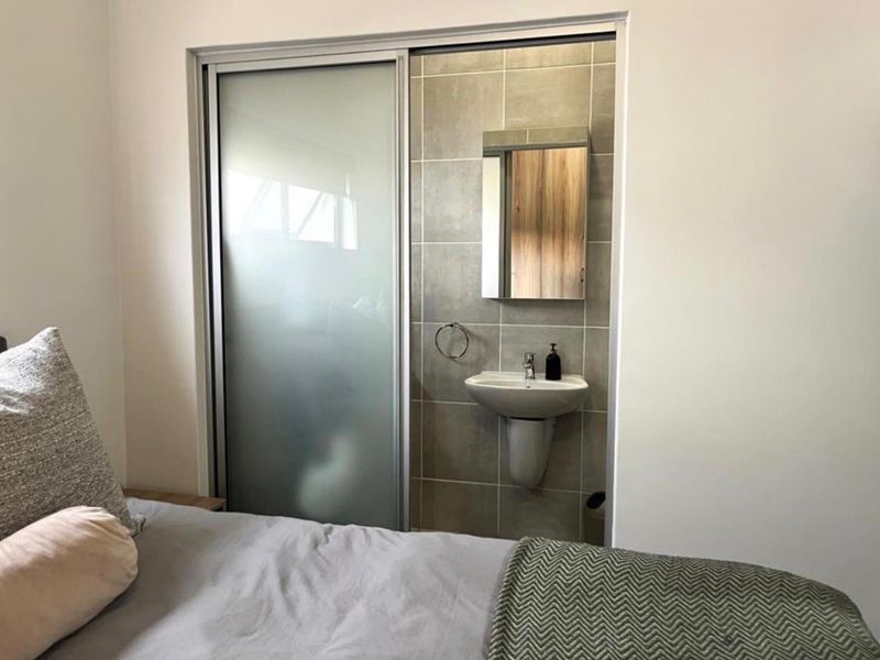 A bedroom featuring an integrated en-suite vanity area with a pedestal basin, tiled splashback, and a sliding glass door partition.